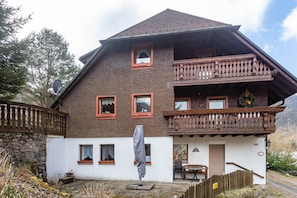 Eine zweistöckige Chalet mit Balkon, Steinmauer und Bergblick.