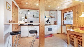 Una cocina con armarios de madera, un comedor con mesa y sillas, y un taburete de bar.