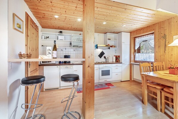 A kitchen with wooden cabinets, a dining area with a table and chairs, and a bar stool.