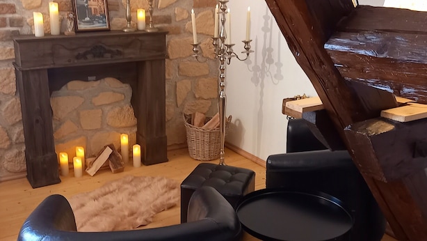 Une pièce chaleureuse avec une cheminée en pierre, un chandelier et un canapé en cuir noir.