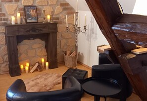 Una habitación acogedora con chimenea de piedra, un candelabro y un sofá de cuero negro.