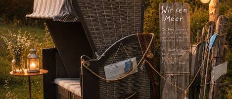 A rustic outdoor seating area with a wicker chair, a small table with candles, and a sign with text.