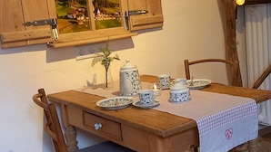 Une table de salle à manger en bois, avec un set de table, un vase contenant une plante et une théière.