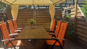 Une table en bois, des chaises orange, une petite plante et, au fond, une clôture en bois.
