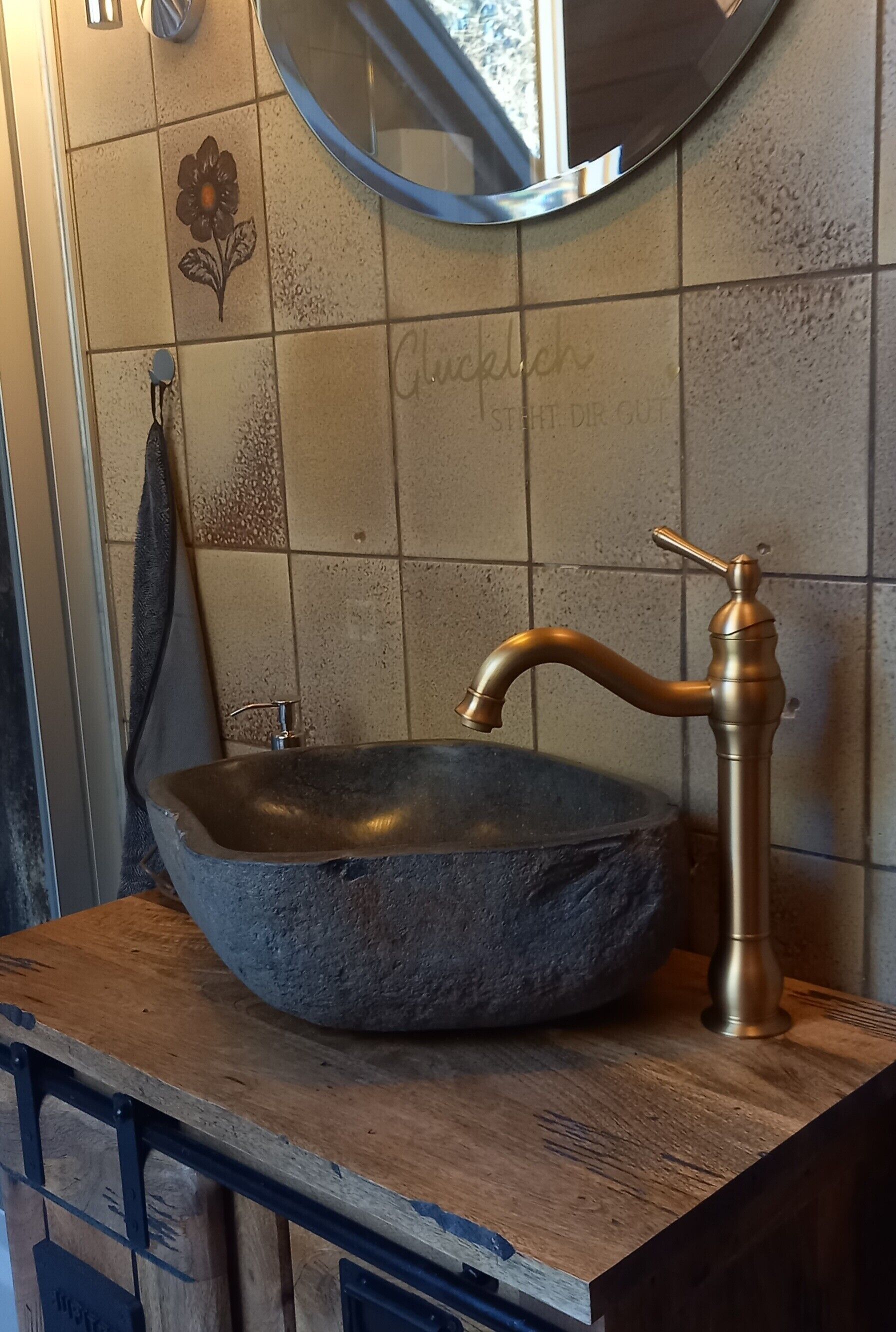 Un baño con un lavabo de piedra, un grifo de bronce, un espejo y un perchero para toallas.
