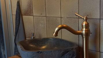 Un baño con un lavabo de piedra, un grifo de bronce, un espejo y un perchero para toallas.
