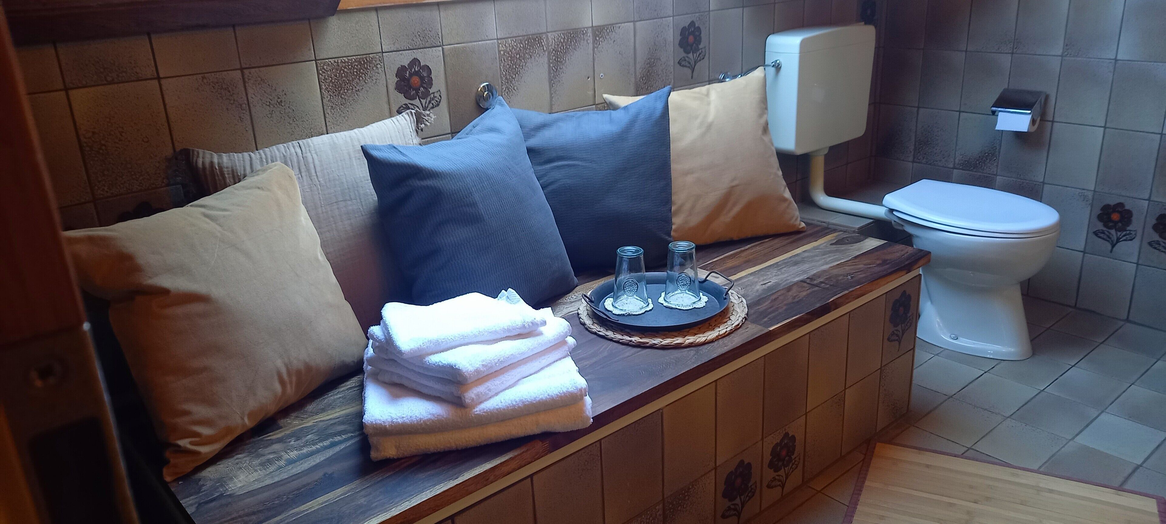 Ein Badezimmer mit einem Holzwaschtisch, einer Toilette und einem Stapel Handtücher.
