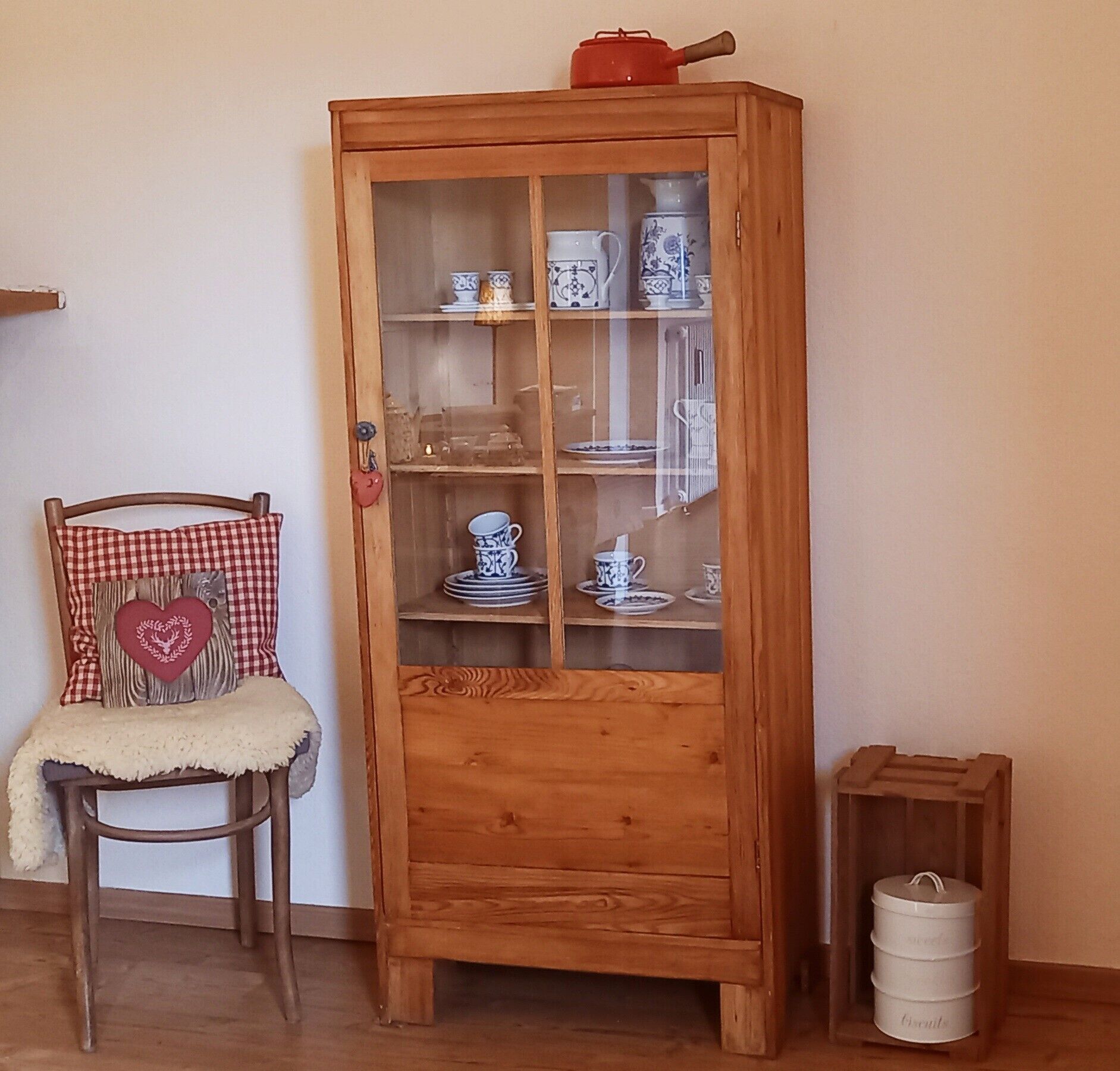 A wooden cabinet with glass doors displaying various dishes and a red teapot on top.