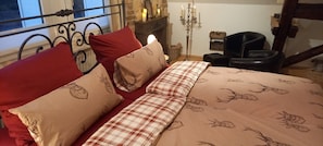 A bed with red and beige pillows, a plaid blanket, a candelabra, and a chair in a room with stone walls and a window. - Country Apartment "Alte Mühle" Near Biggesee (Drolshagen-Berlinghausen)