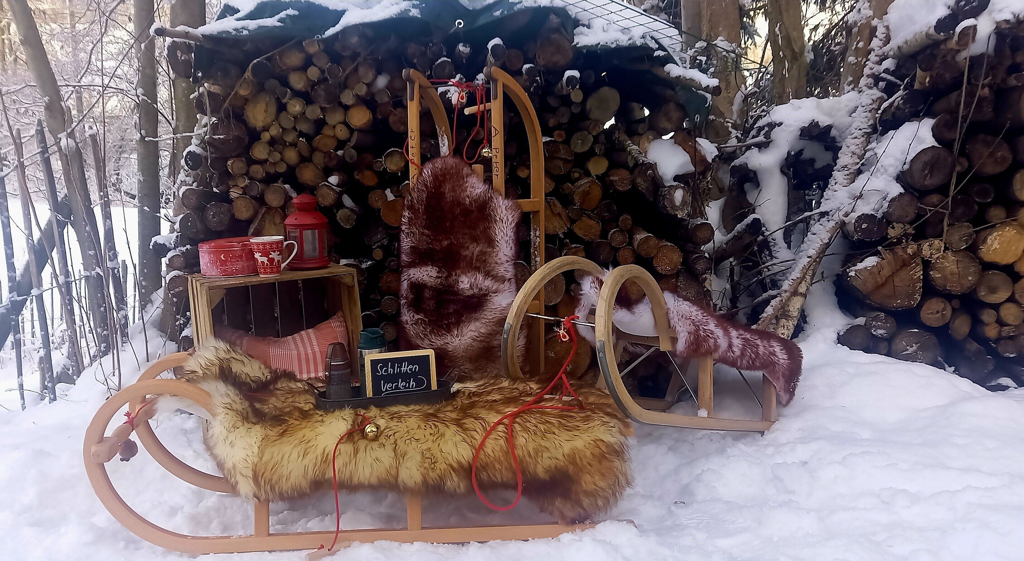 A sled with a fur seat and a sign reading 'Schlittchen Verleih' in a snowy outdoor setting.