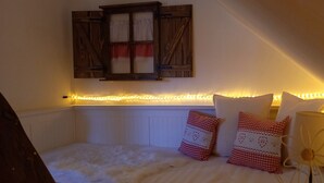 Une chambre avec un plafond en pente, une fenêtre avec des volets, un lit avec une literie blanche et des coussins décoratifs.