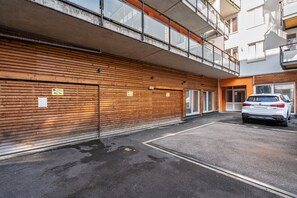 Ein mehrstöckiges Gebäude mit Holzfassade, einem überdachten Parkbereich und einem weißen Auto darin.