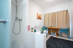 Ein Badezimmer mit Dusche, einem Bett, einem Nachttisch mit Pflanze und einem Fenster mit Vorhängen.