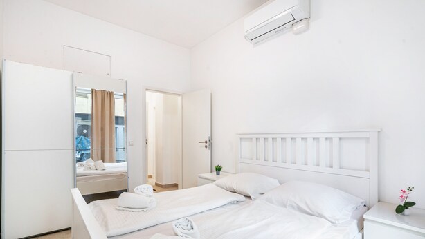 A hotel room with two beds, a mirror, a bedside table with a plant, and a white wardrobe. - Aldars Urban Trio Suite No. 9 with Wi-Fi and Air Conditioning (München)