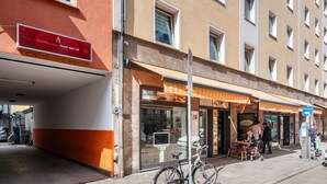 A building with a red and white sign, a bicycle, and a stroller on the sidewalk. - Aldars Urban Trio Suite No. 9 with Wi-Fi and Air Conditioning (München)