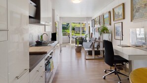 A modern kitchen with white cabinetry, a dining area with a black chair, and a view of a garden through a glass door.