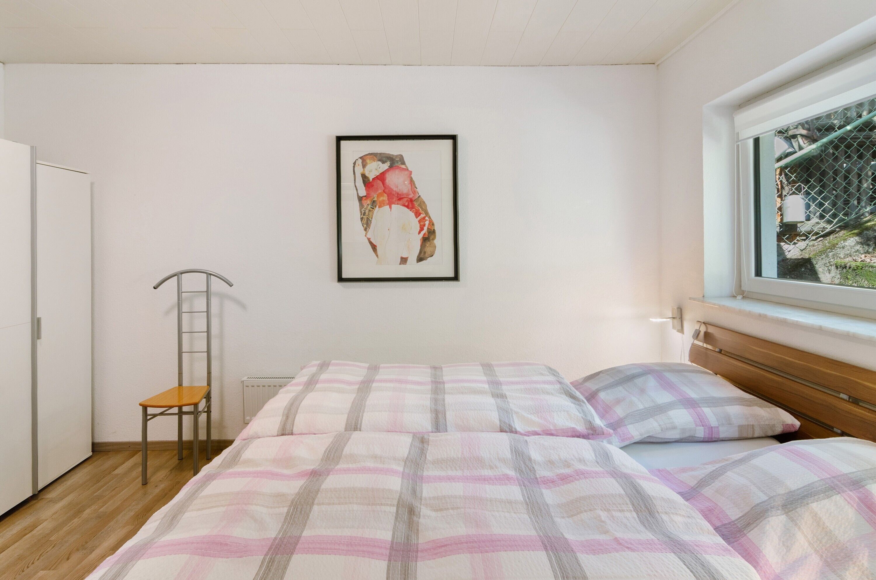 A bedroom with a bed, a chair, a radiator, and a window.