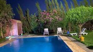 Een zwembad met ligbedden en een kleine tuinhuis in een achtertuin.