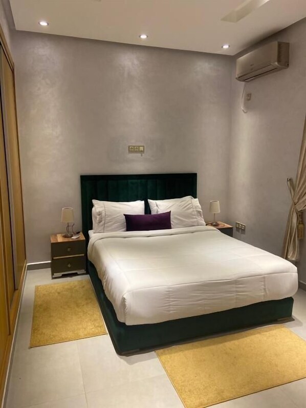 A modern bedroom with a large bed, two bedside tables, and a wall-mounted air conditioner.