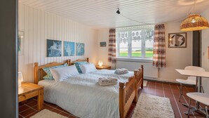 Une chambre à coucher comprenant un lit, des tables de chevet, une fenêtre avec des rideaux, un luminaire suspendu et une vue sur l’extérieur.