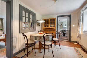 Un coin repas comprenant une table ronde, quatre chaises, un luminaire suspendu et un buffet en bois doté de portes en verre.