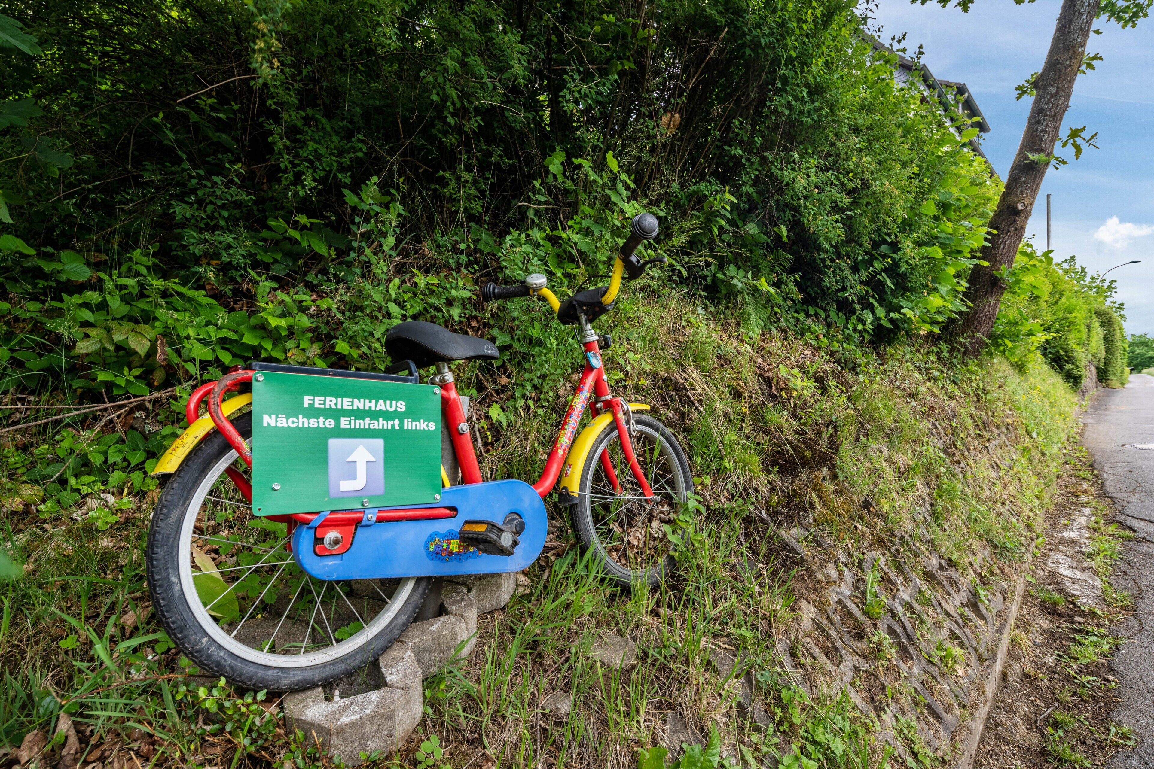 Uma bicicleta estacionada em um muro de pedra ao lado de uma estrada, com uma placa verde presa.