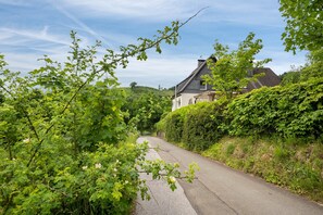 A narrow road flanked by lush greenery and a stone house with a pitched roof. - Holiday Home 'Maag, 102qm' with Private Terrace and Wi-Fi (Attendorn)