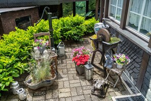 Um jardim com plantas em vasos, uma cadeira de madeira, um candeeiro e uma estátua.