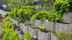 A garden with various plants and flowers, a wooden fence, and a house in the background. - Holiday Home 'Maag, 102qm' with Private Terrace and Wi-Fi (Attendorn)