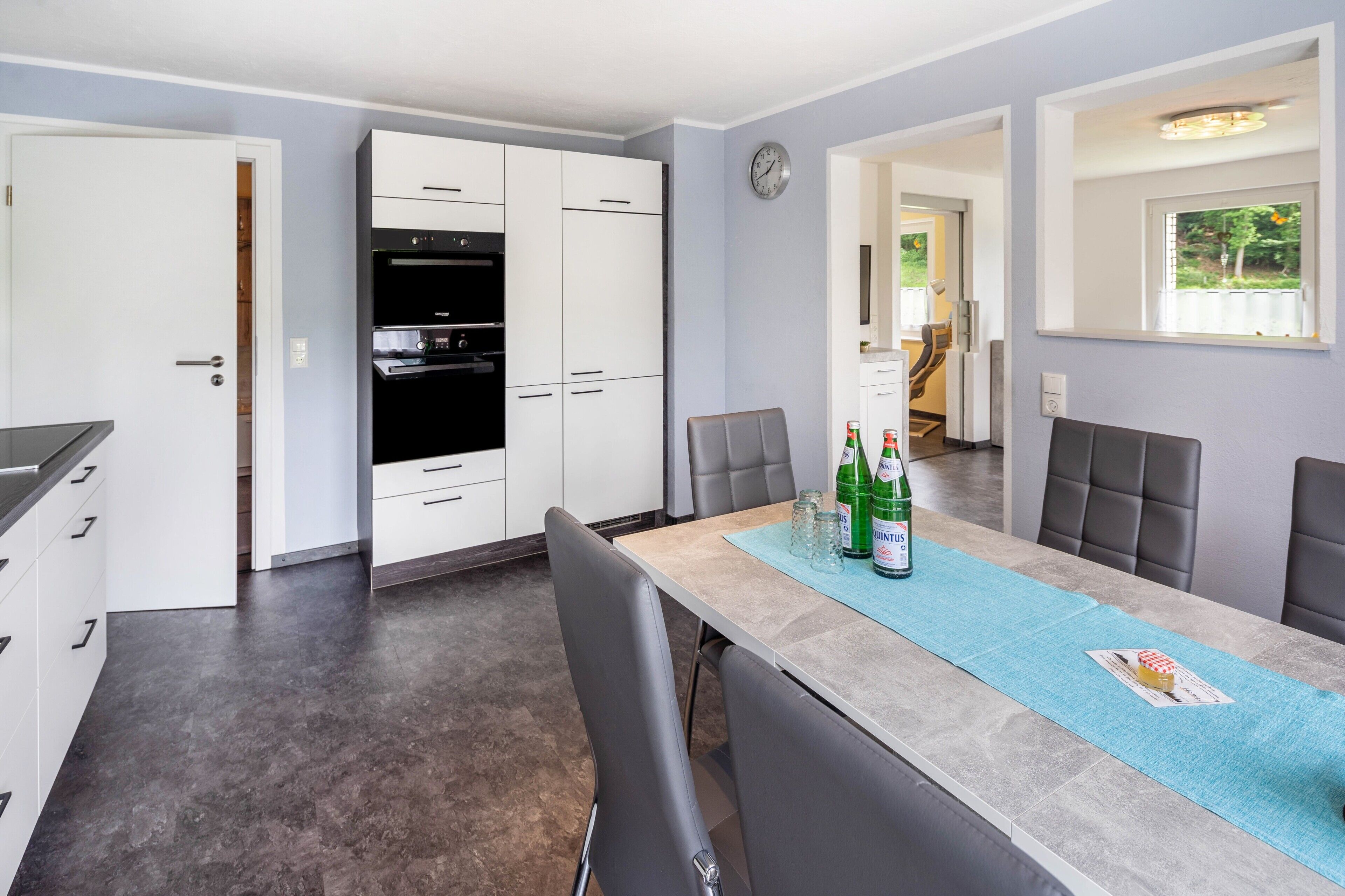A modern kitchen with white cabinets, a black oven, and a dining area with a table set for four.