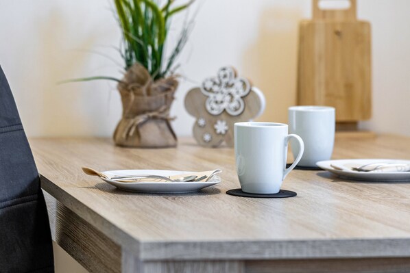 A wooden table with a white mug, a plate with a spoon, and a small plant in the background.