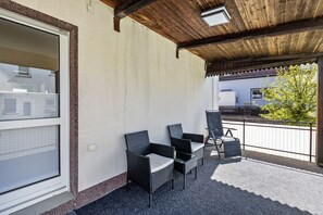 An outdoor patio with wicker furniture, a wooden ceiling, and a view of a building in the background.