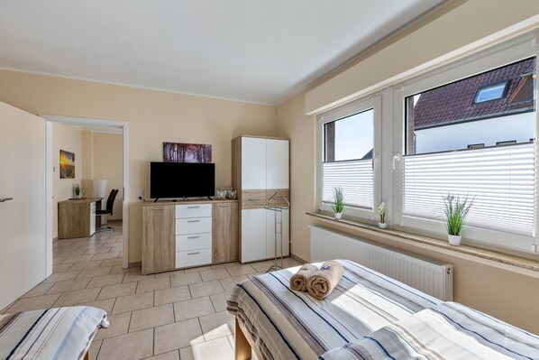 A bedroom with a bed, a TV, a wardrobe, a desk, and a window with blinds.