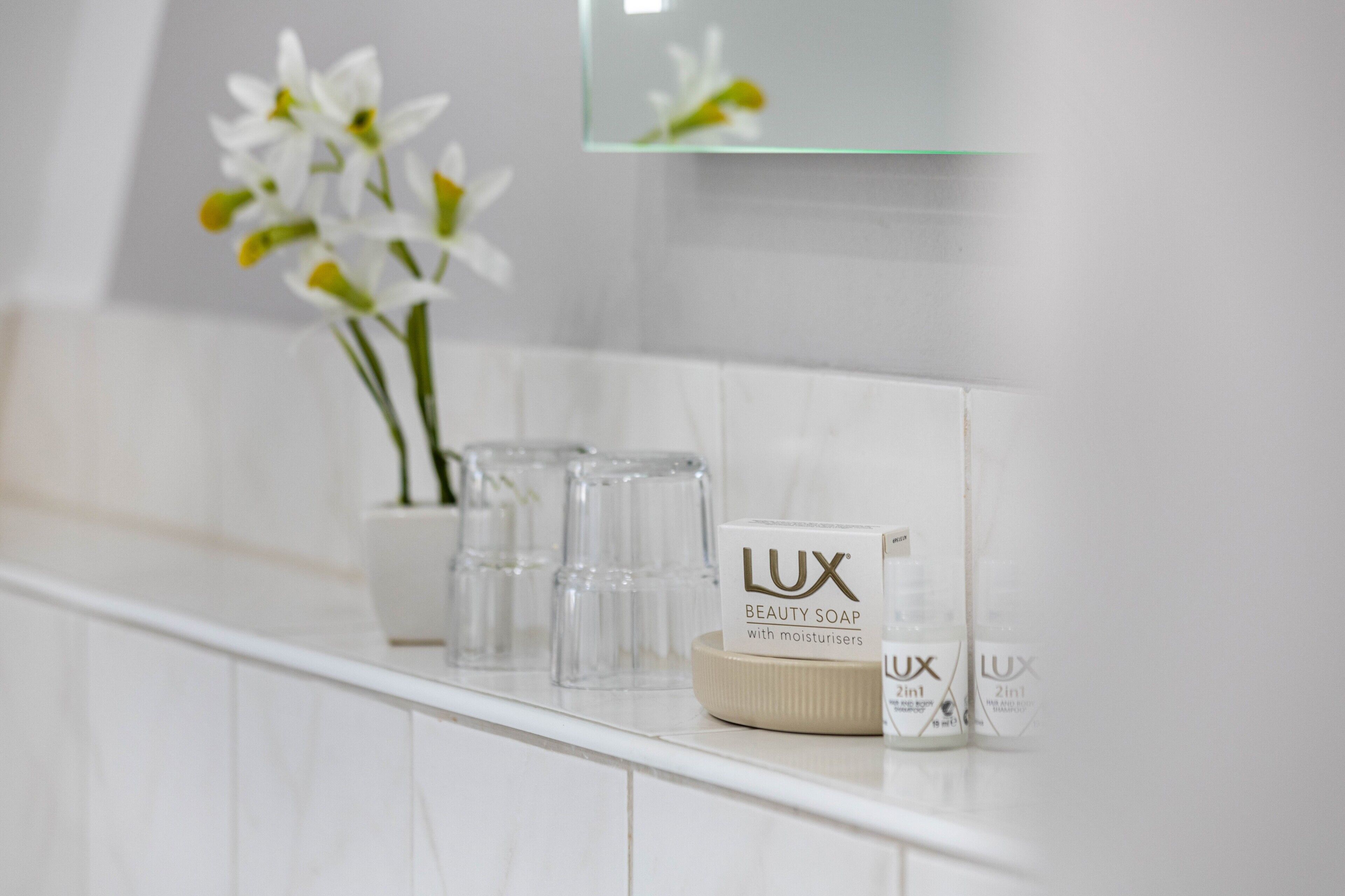 A bathroom with white tiles, a mirror, and two bottles of LUX beauty soap.