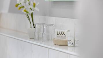 A bathroom with white tiles, a mirror, and two bottles of LUX beauty soap.