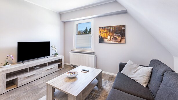 A modern living room with a flat-screen TV, wooden entertainment unit, a grey sofa, and a window with blinds. - Wimbern Apartment 'Upper Floor' with Streaming, Kitchen & Laundry (Wickede (Ruhr))