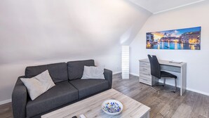 A modern living room with a grey sofa, a wooden coffee table, a desk with a chair, and a cityscape painting on the wall. - Wimbern Apartment 'Upper Floor' with Streaming, Kitchen & Laundry (Wickede (Ruhr))