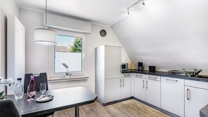 A modern kitchen with white cabinets, a dining table with chairs, a window with blinds, and a clock on the wall. - Wimbern Apartment 'Upper Floor' with Streaming, Kitchen & Laundry (Wickede (Ruhr))