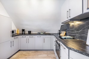 A modern kitchen with white cabinets, a black marble backsplash, and stainless steel appliances.