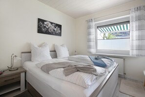 Une chambre à coucher avec un lit, une table de chevet, une lampe, une fenêtre avec des rideaux et un radiateur.