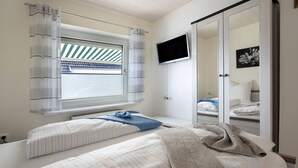 Ein Schlafzimmer mit zwei Betten, einem Fernseher, einem Fenster mit Vorhängen und einer Schiebetür.