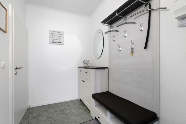 Un baño con tocador blanco, espejo, banco y ducha con barra para toallas.