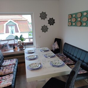 Een eethoek met een tafel voor vier personen, een bank met bloemenkussens en decoratieve wandkunst.
