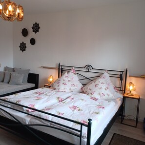 Een net opgemaakt bed met bloemenbeddels, een nachtkastje met een lamp en decoratieve wandkunst.