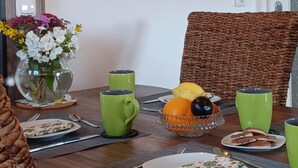 Uma mesa de jantar com um vaso de flores, chávenas verdes, uma fruteira e pratos.