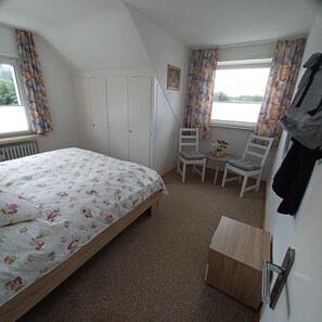 A bedroom with a bed, a chair, a small table, a radiator, and a window with curtains. - Apartment 'Walli Og' with Mountain View, Private Garden and Wi-Fi (Goslar)