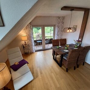 Ein gemütliches Loft-Zimmer mit Esstisch, Korbstühlen, einer Couch und einer Lampe.