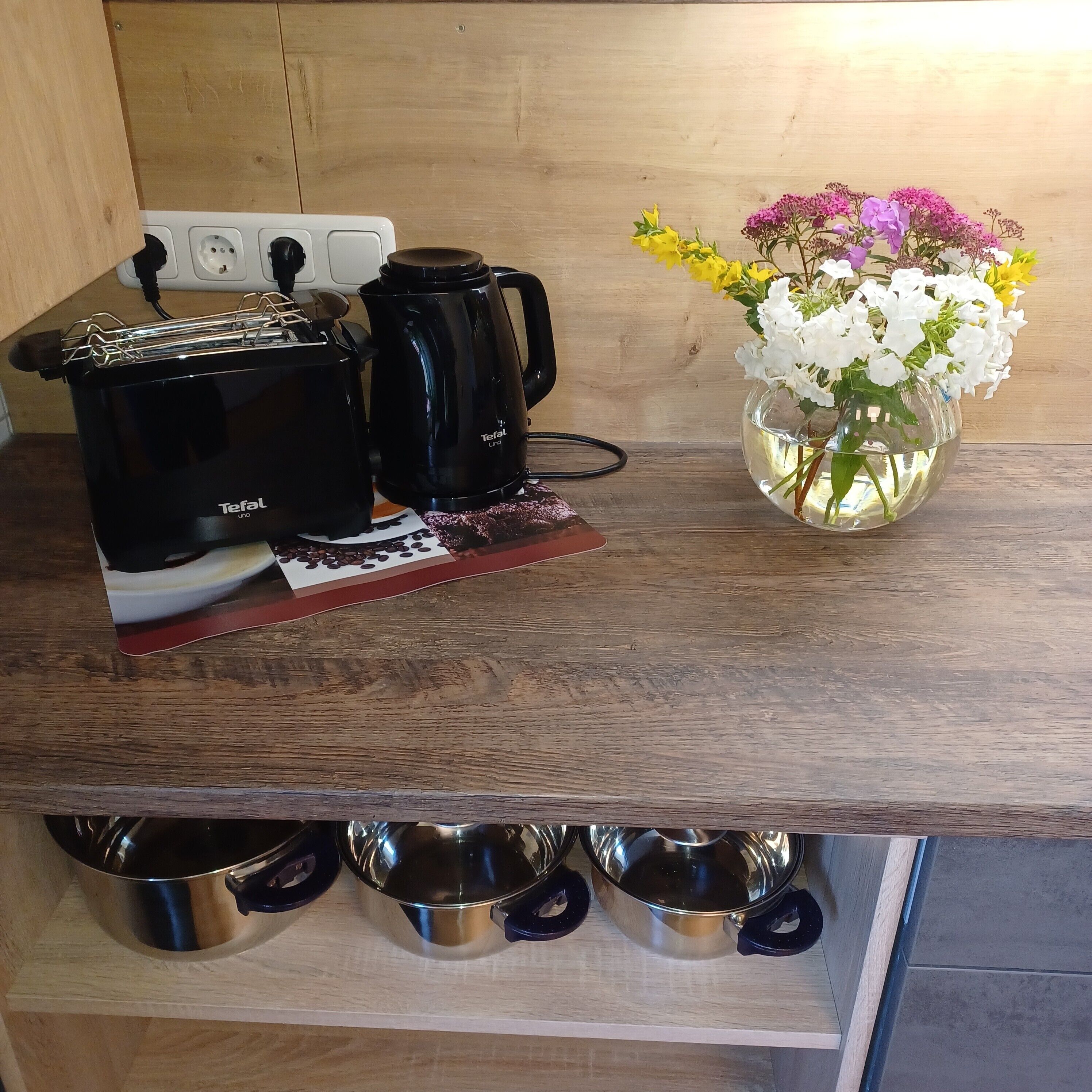 A kitchen counter with a coffee maker, a kettle, and a vase with flowers.