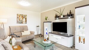 A modern living room with a sofa, glass coffee table, flat-screen TV, and a cabinet with glass doors. - Apartment 'Landblick' with Shared Garden, Balcony and Wi-Fi (Homberg (Efze))