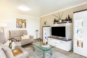 Moderni olohuone, jossa on sohva, lasinen sohvapöytä, litteänäyttöinen televisio ja lasiovilla varustettu kaappi.